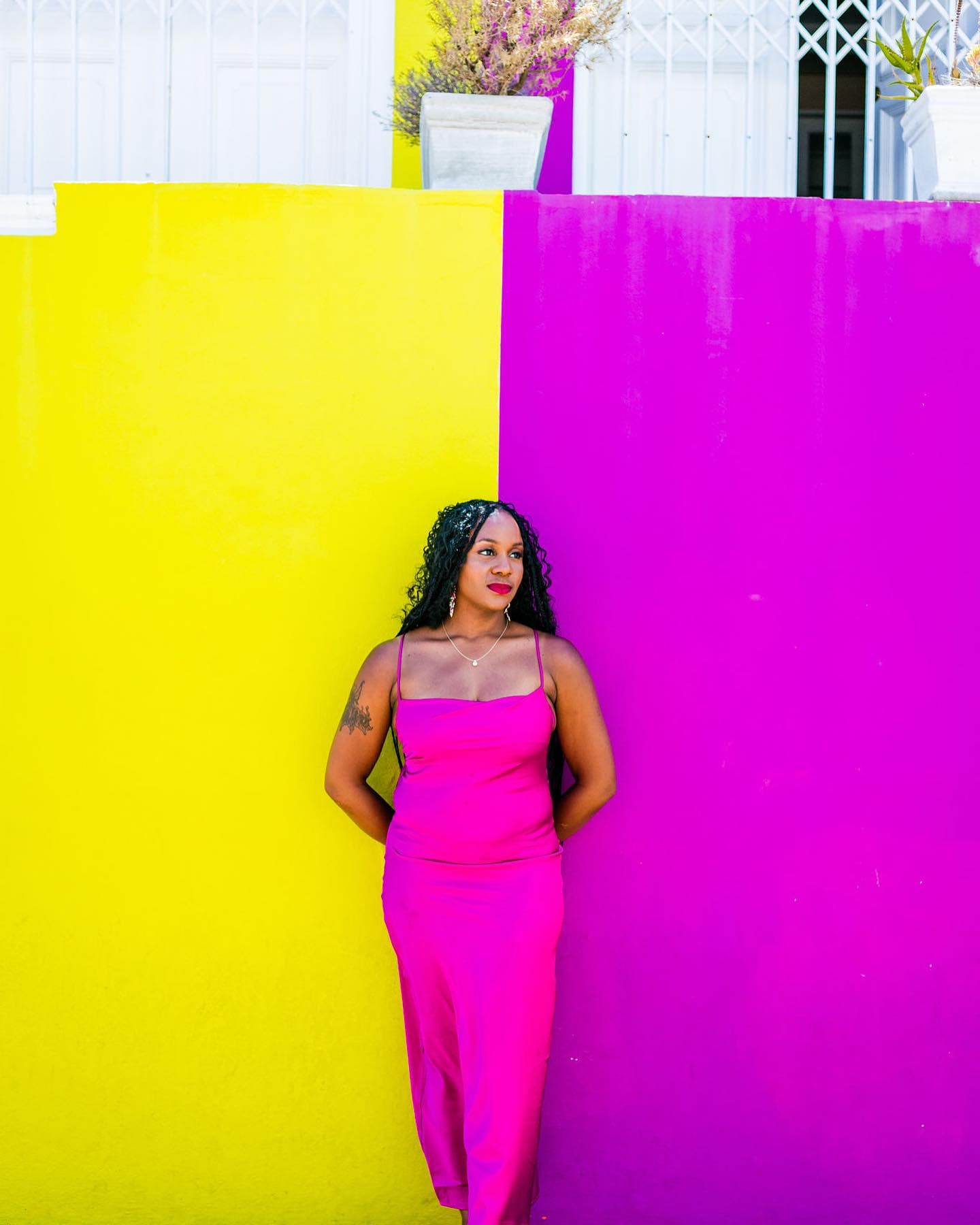 Neké Akua in a pink slip dress against the split yellow-and-magenta walls of Bo-Kaap, Cape Town.