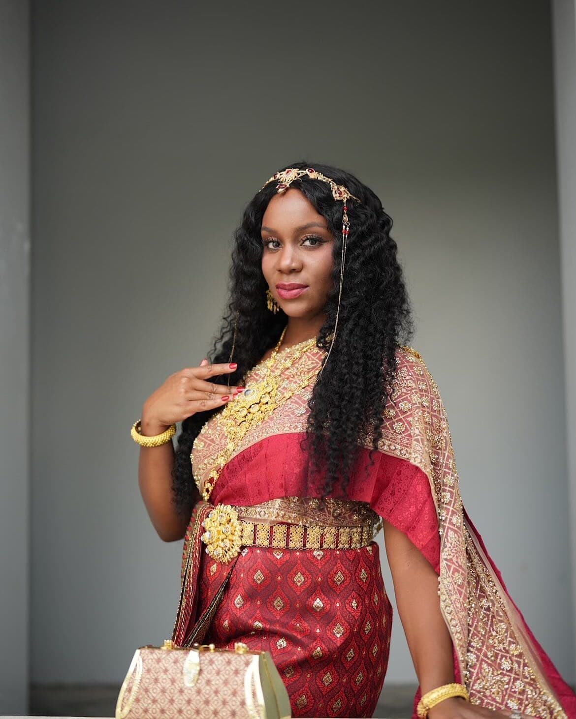 Neké Akua in an elaborate red-and-gold traditional dress with a jeweled headpiece.