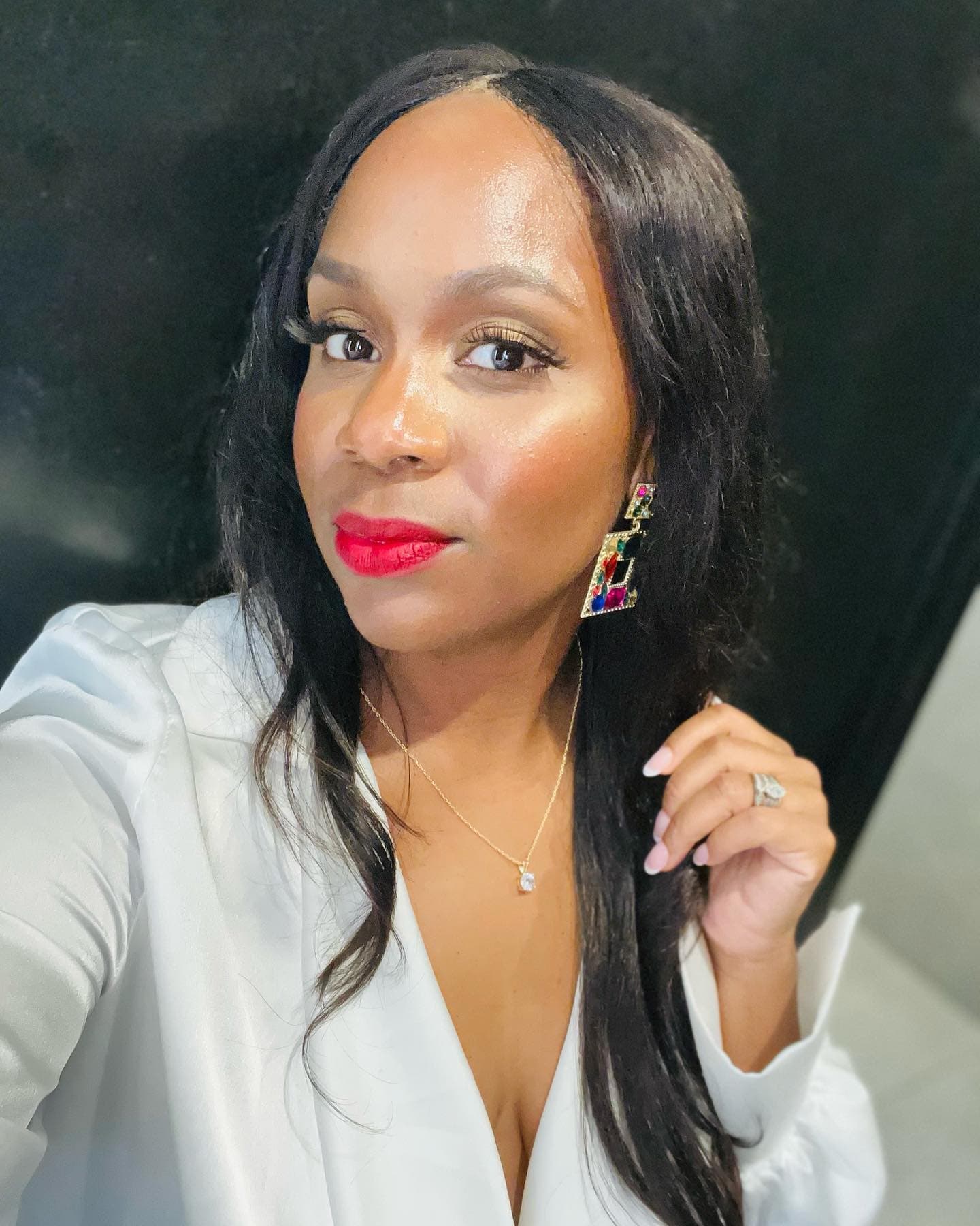 Neké Akua in a white satin blazer and red lip, a jewelled geometric earring framing her face.