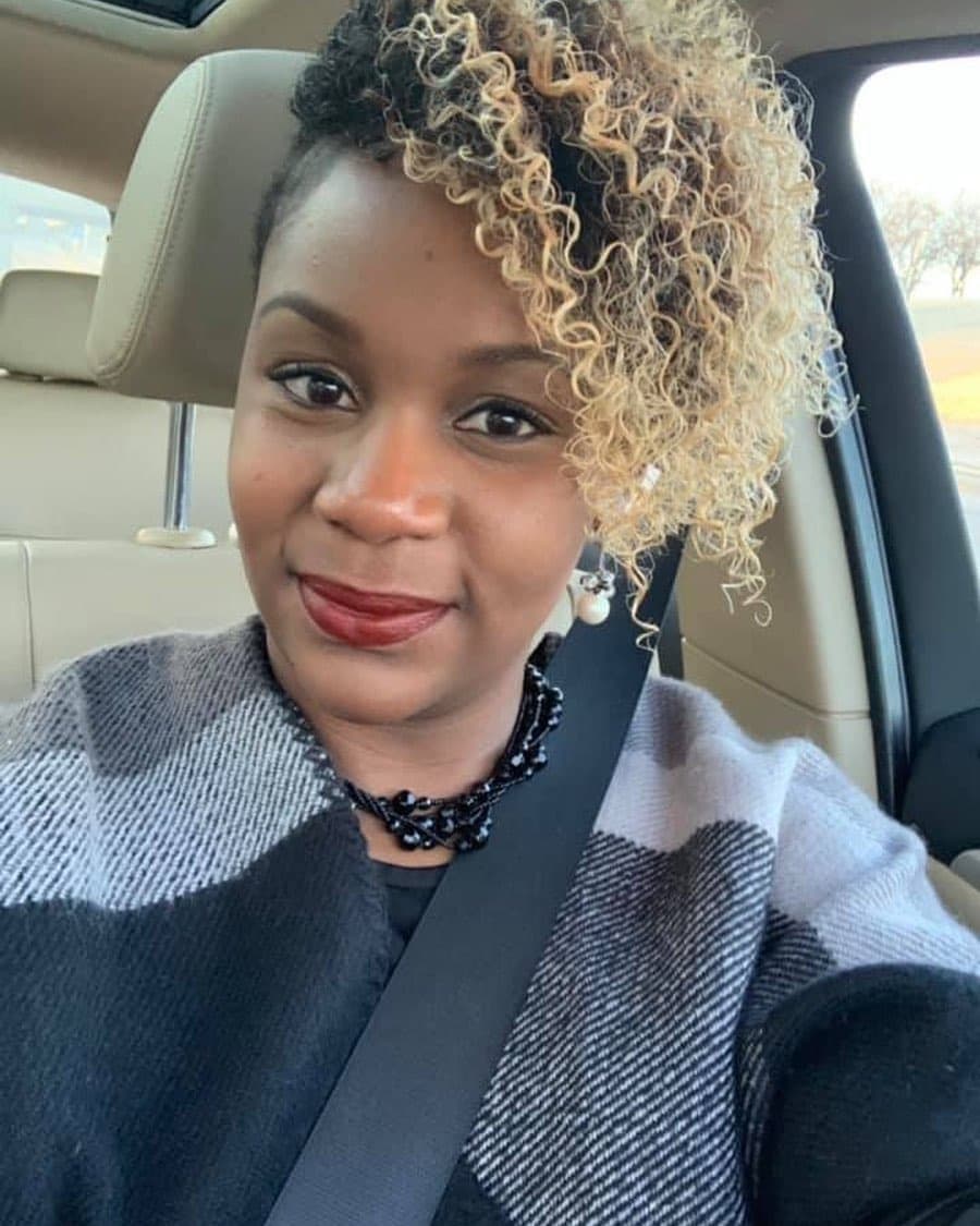 Neké Akua in a grey colour-blocked wool coat and beaded necklace, blonde curls swept into a high ponytail.