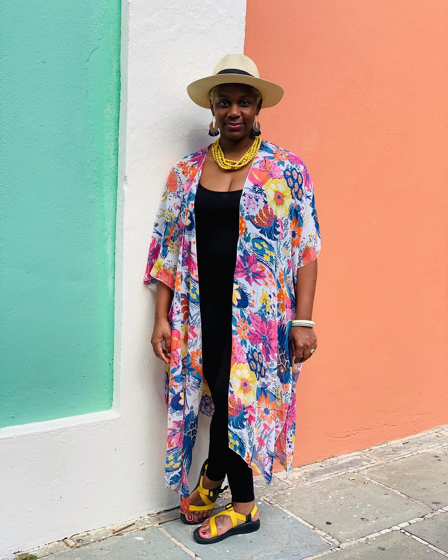 Neké Akua in a floral kimono and sun hat against a teal-and-coral wall.