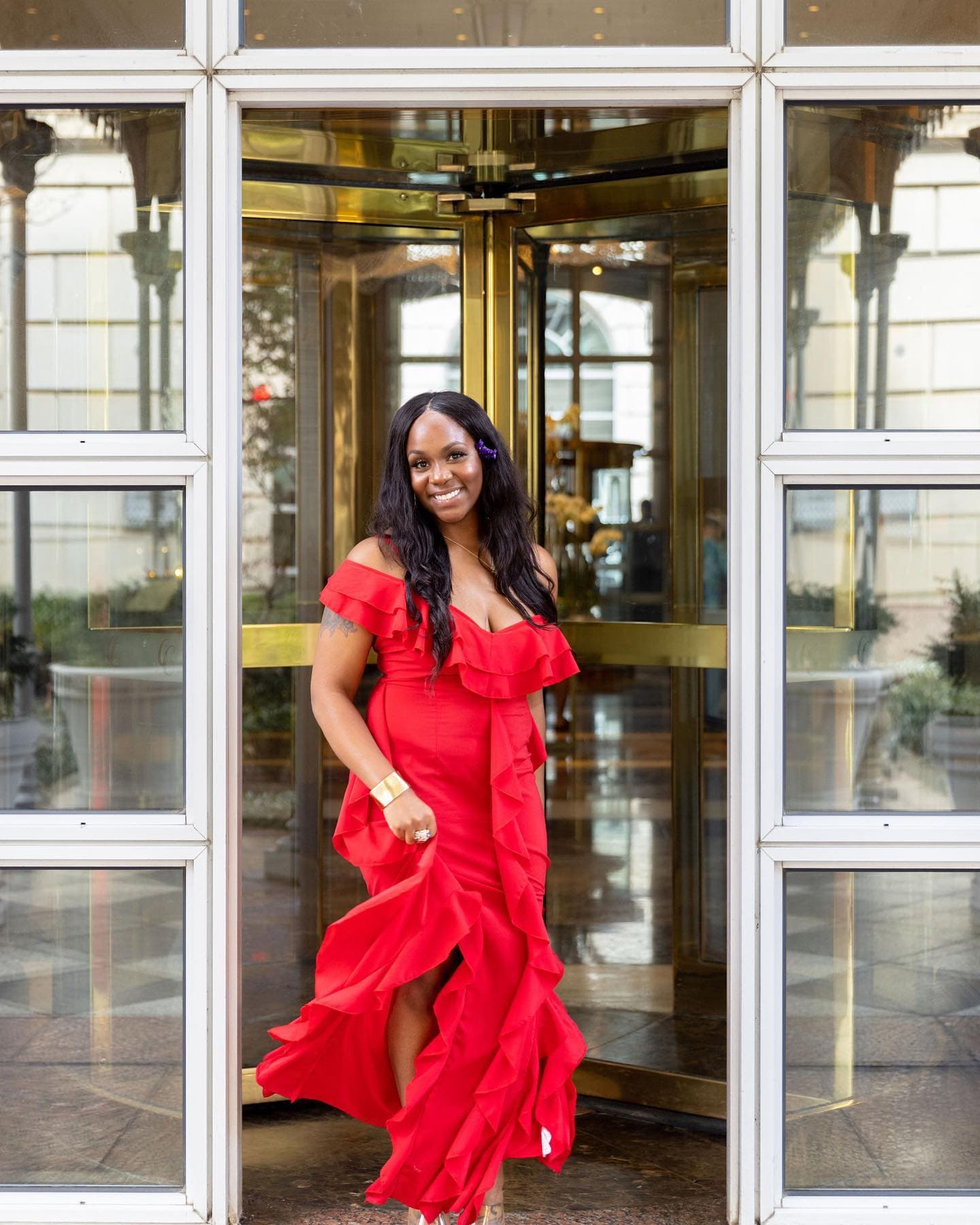Neké Akua in a red ruffled gown at a hotel's brass revolving-door entrance.