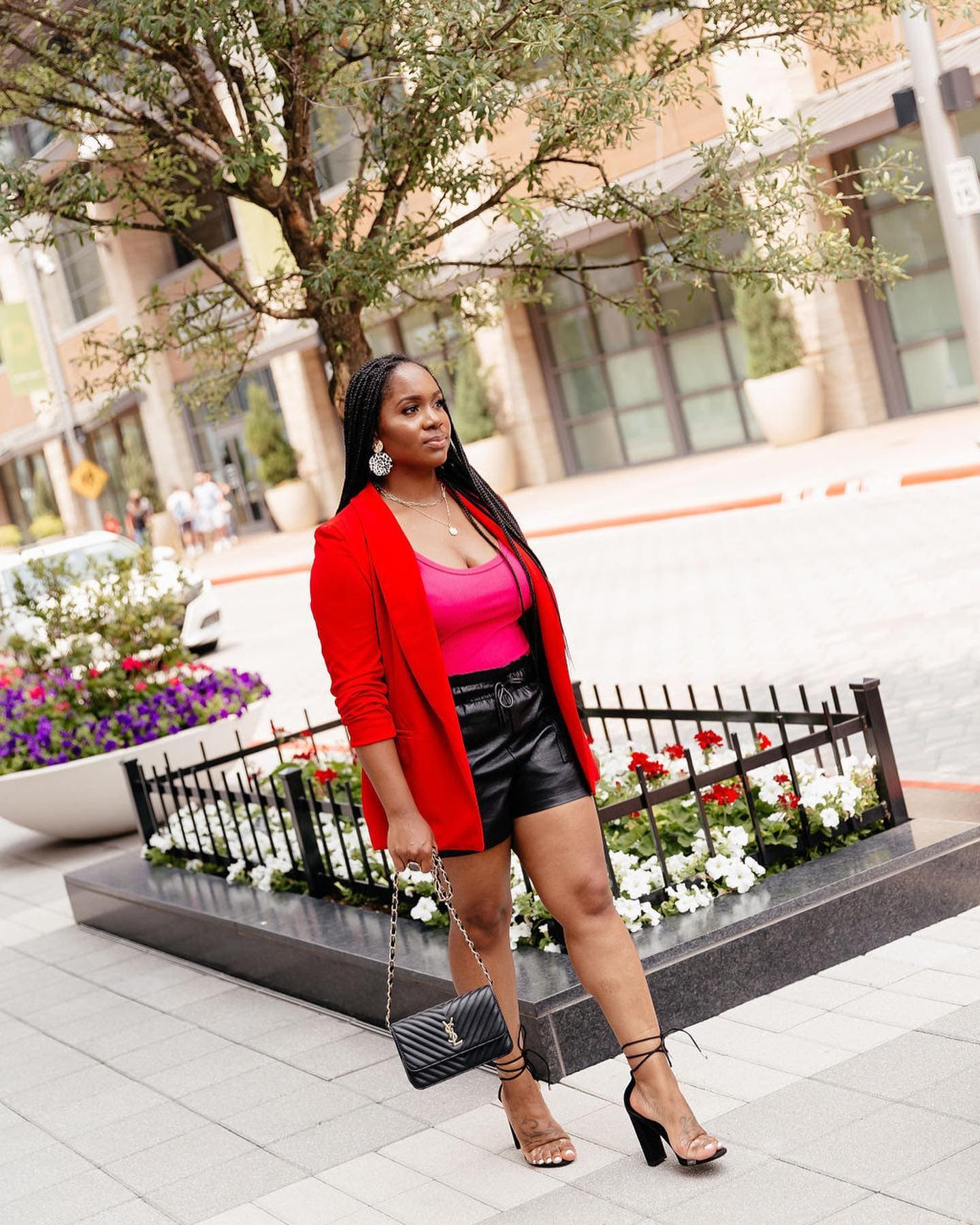 Neké Akua in a red blazer and pink top, holding a quilted bag beside a flower planter.