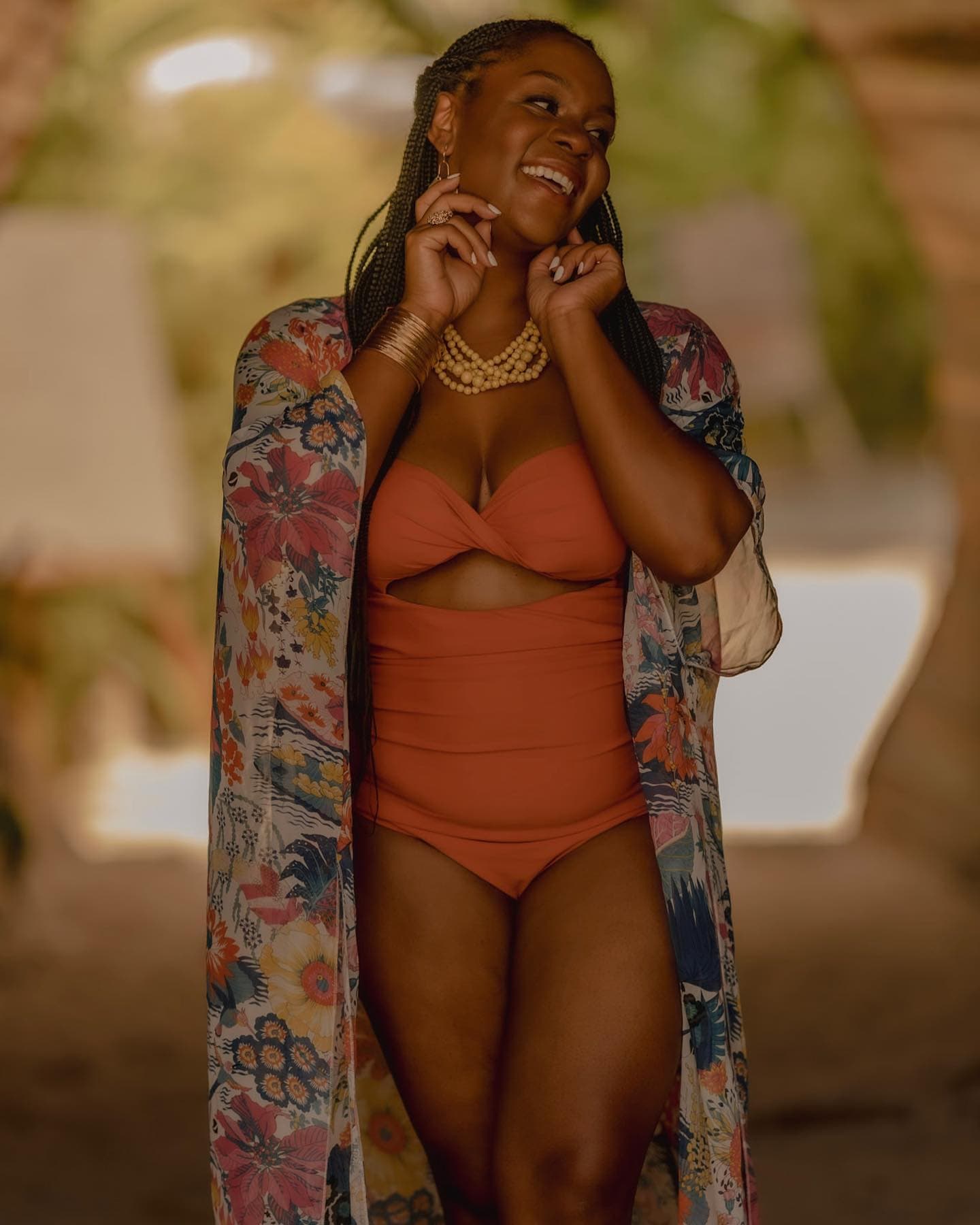 Neké Akua laughing poolside in a rust-orange cut-out swimsuit and floral kimono.
