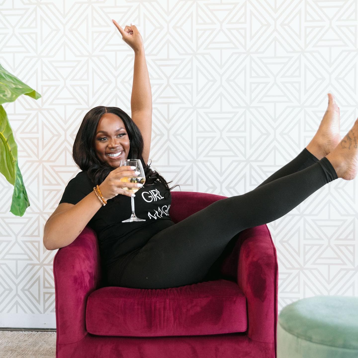 Neké Akua kicked back in a burgundy velvet armchair with a glass of white wine.