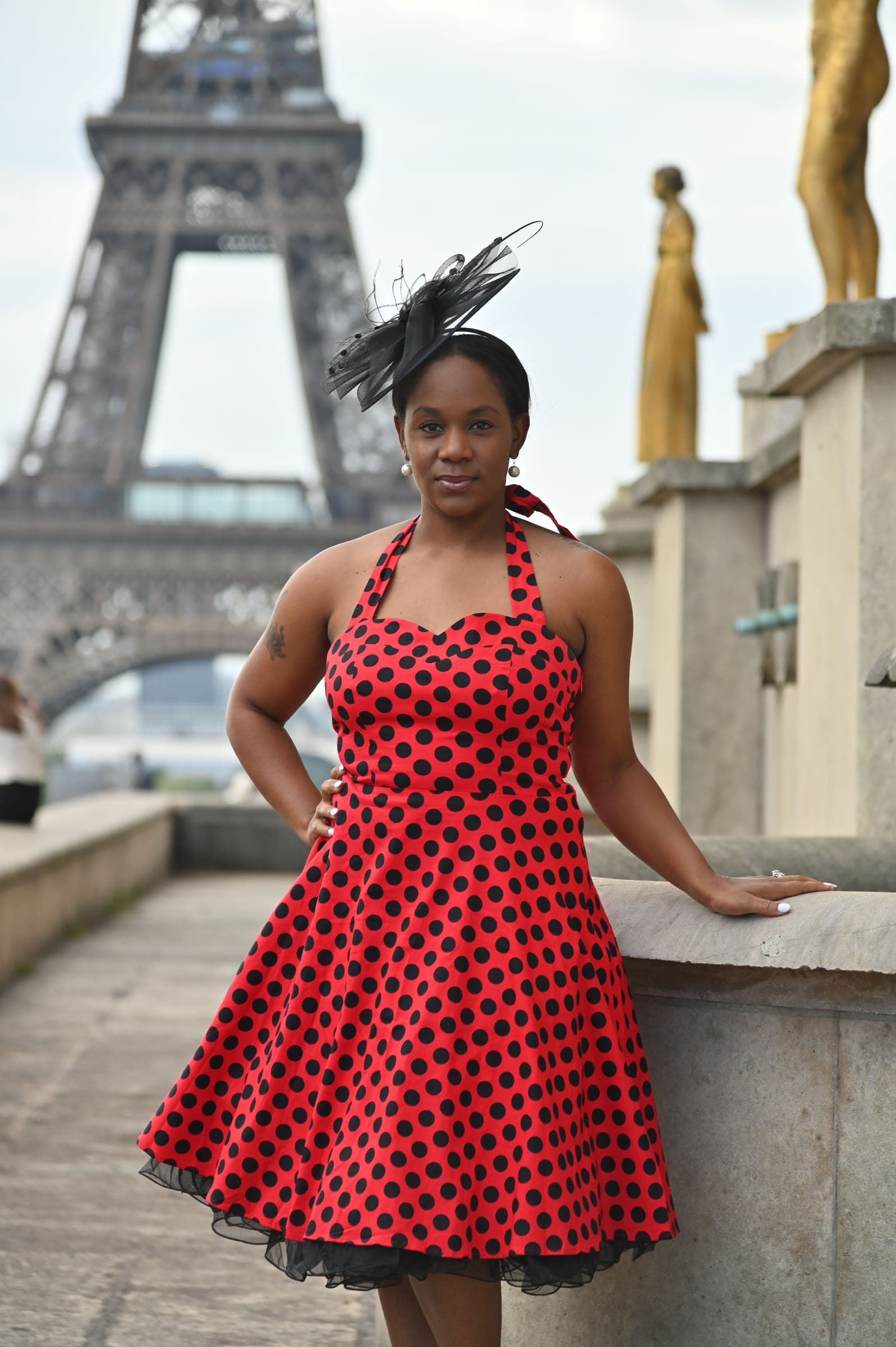 Neké Akua leaning on the Trocadéro's stone balustrade in a red polka-dot dress, the Eiffel Tower over her shoulder.
