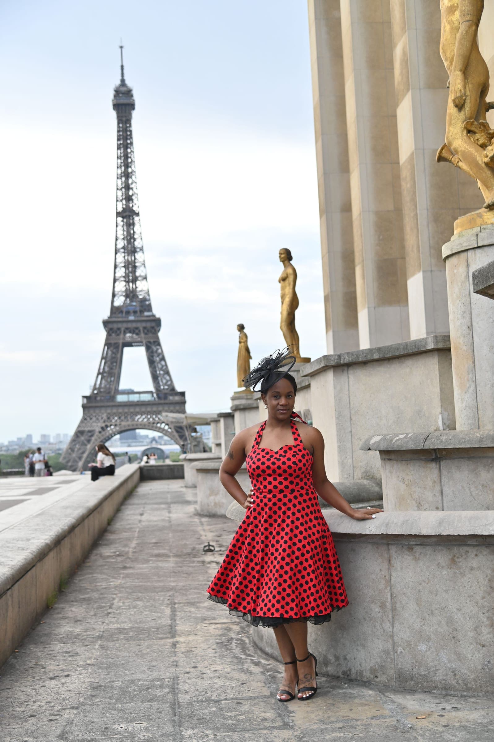 Neké Akua on the Trocadéro steps in a red polka-dot dress, the terrace's gilded statues beside her and the Eiffel Tower across the river.