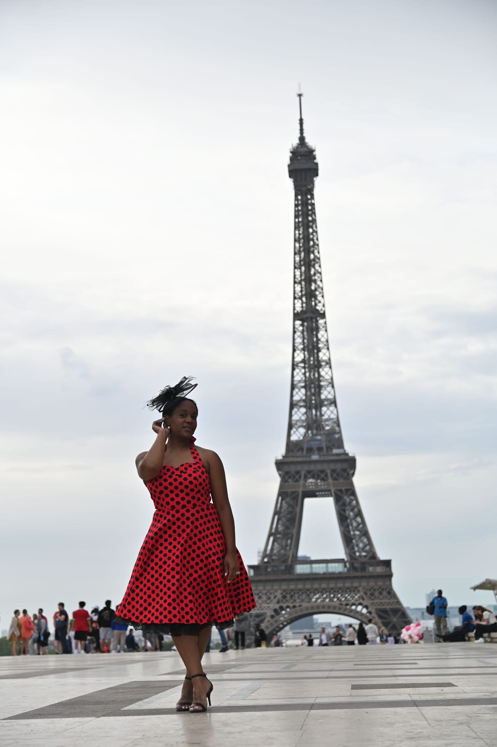 Neké Akua in a red polka-dot dress crossing the Trocadéro esplanade, the whole of the Eiffel Tower rising behind her.