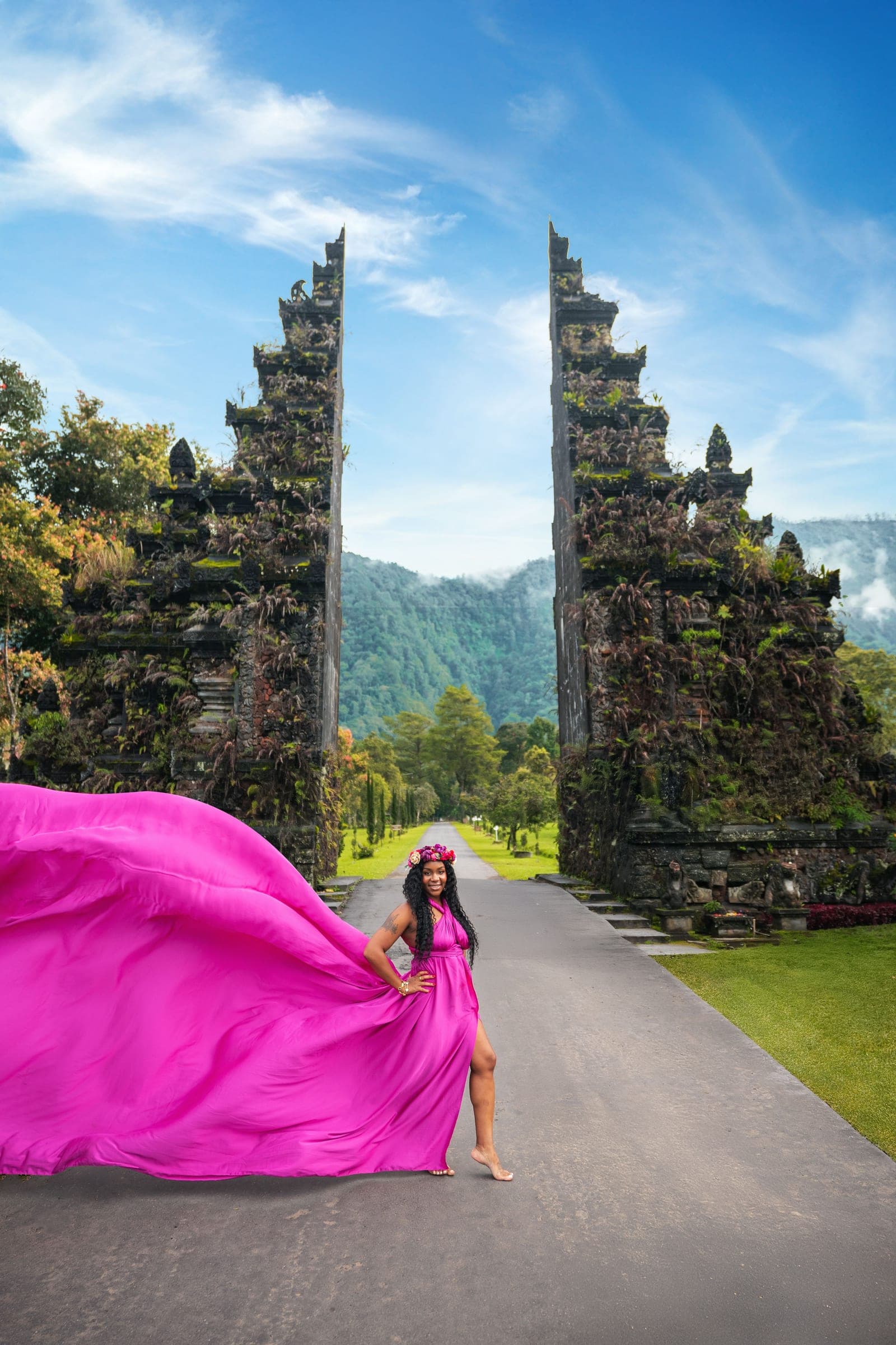 Neké Akua standing in the gap of Bali's Handara Gate, magenta fabric caught mid-air across the frame with the mountains beyond.