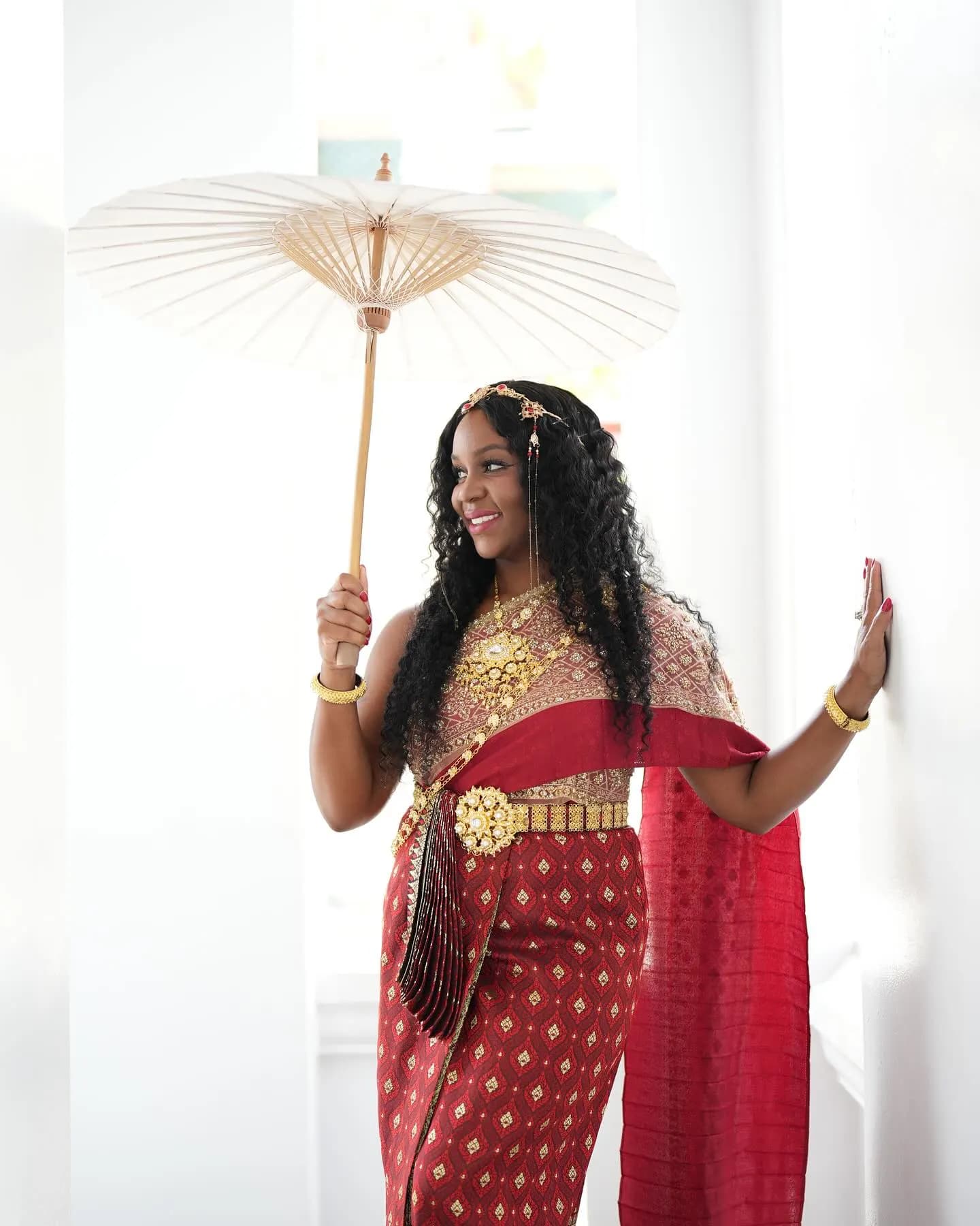 Neké Akua in a red-and-gold gown holding a paper parasol.